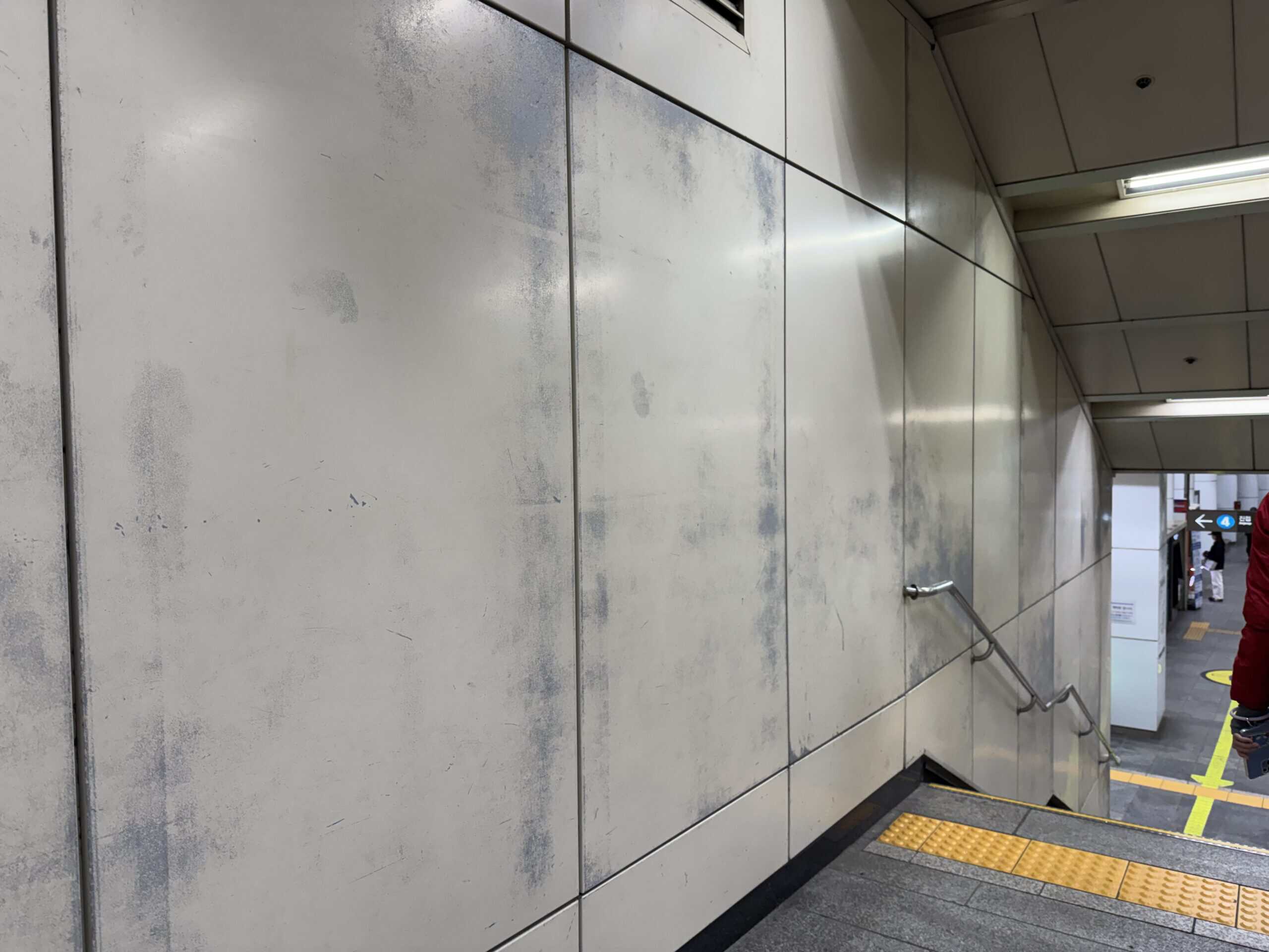 捷運站樓梯間傳統烤漆金屬牆面板因乘客每日頻繁接觸摩擦導致塗層嚴重磨耗與退色